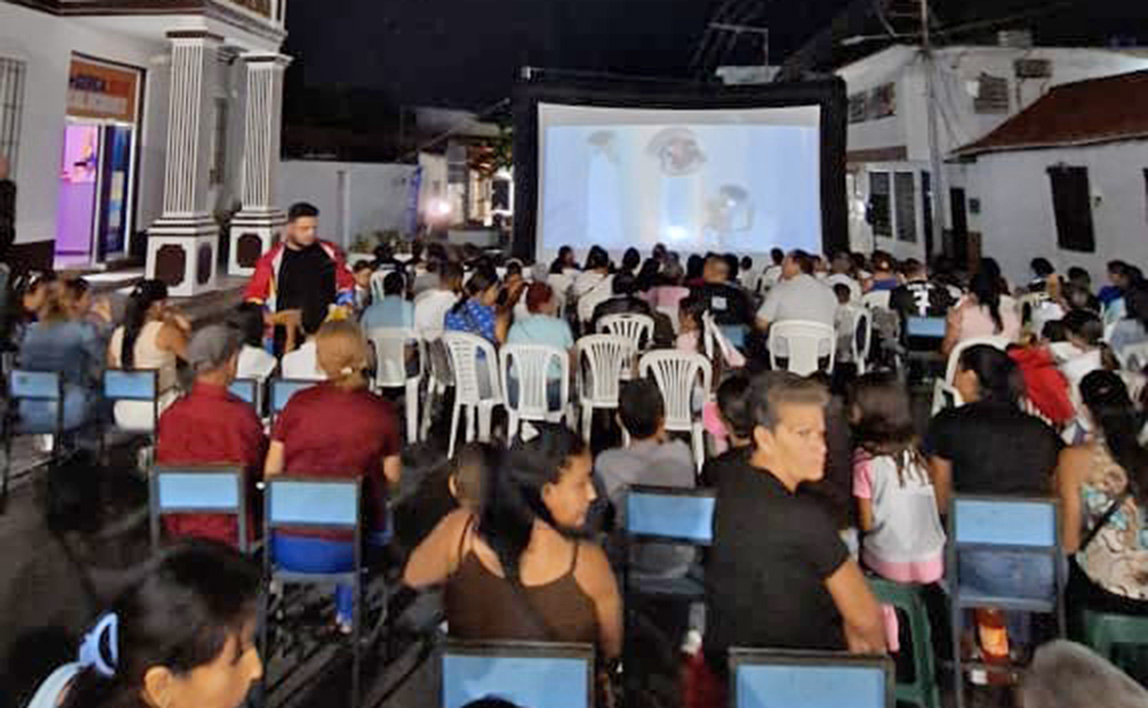 Asistentes sentados en sillas, frente a la pantalla inflable para la proyección de cine bajo las estrellas, ALUCINE en el municipio Revenga. Edo Aragua