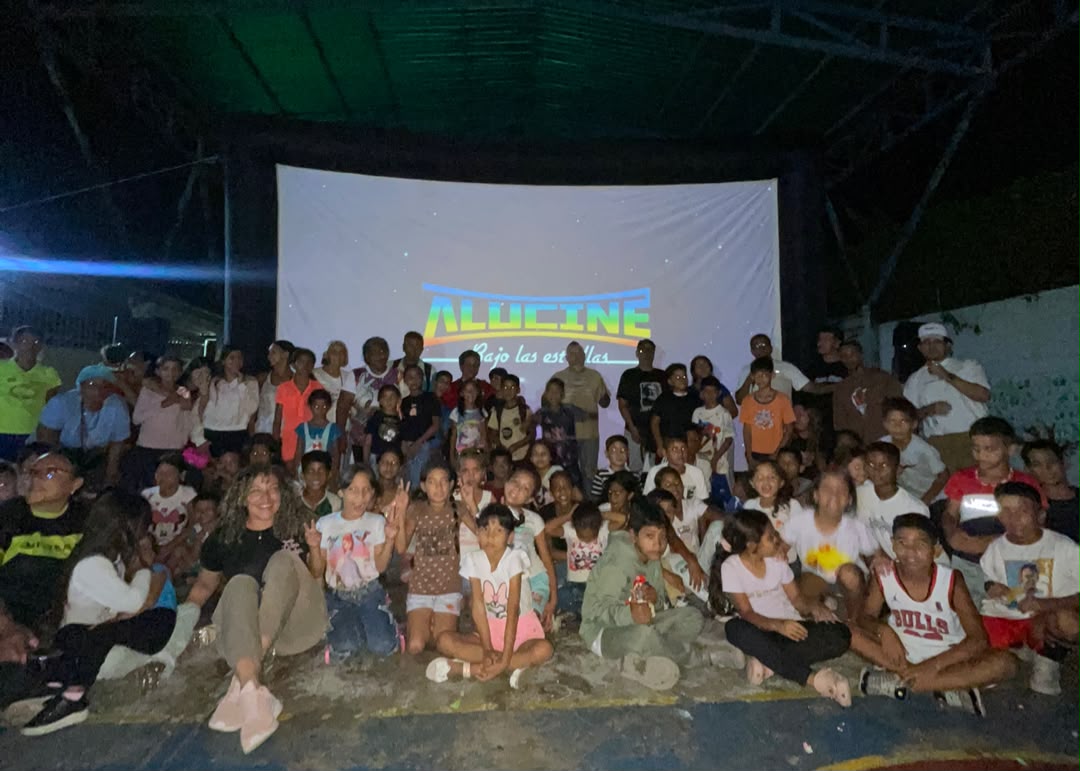 niñas y niños de san mateo reunidos para una foto grupal frente a la pantalla de cine móvil con el emblema de ALUCINE
